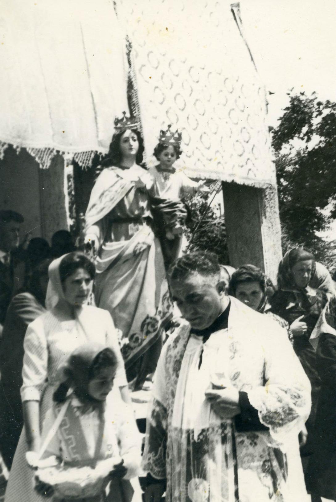 Adele with a priest in front of a statue of the Madonna.