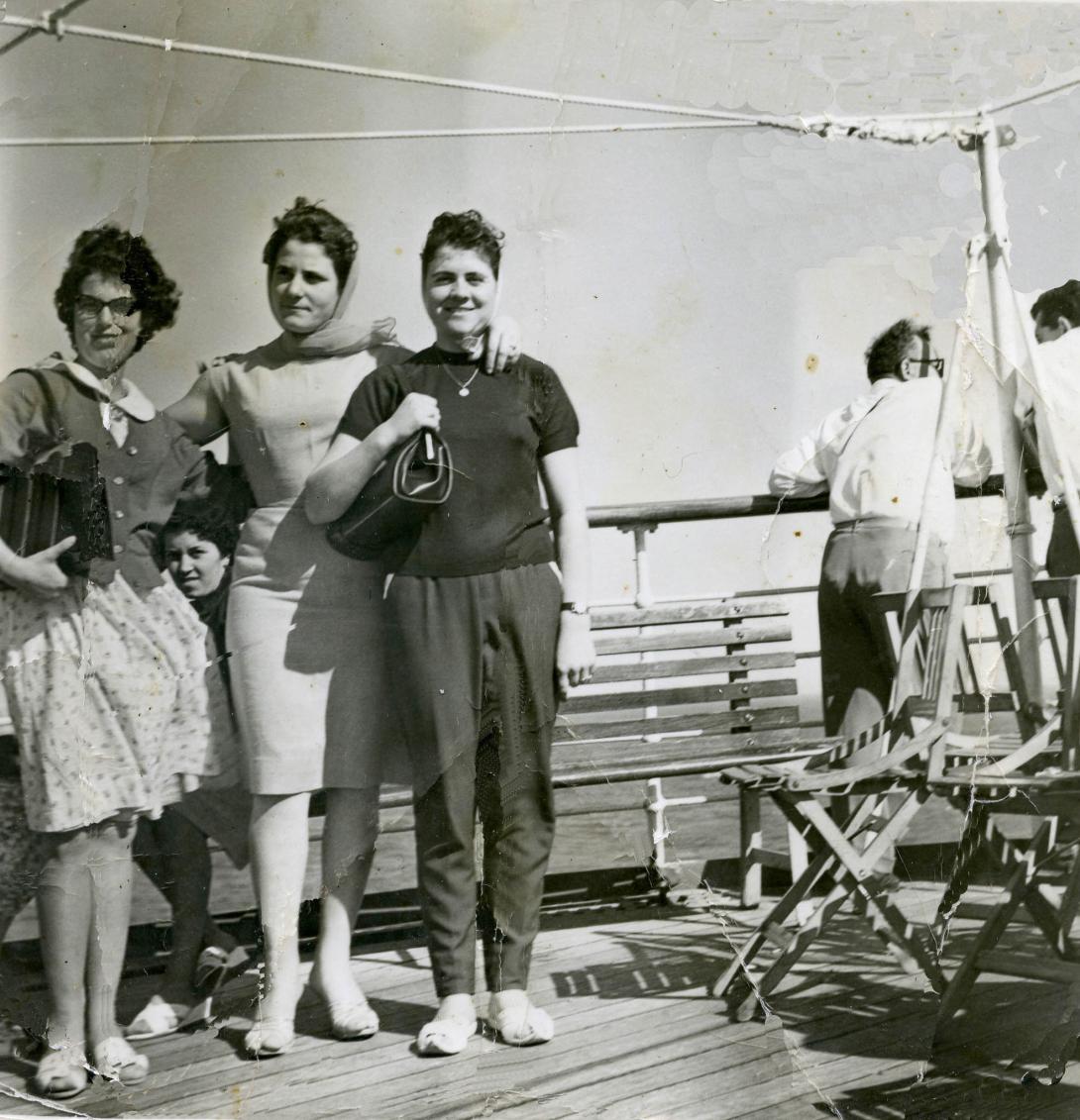 Three women smiling in front of the railing of a passenger ship.