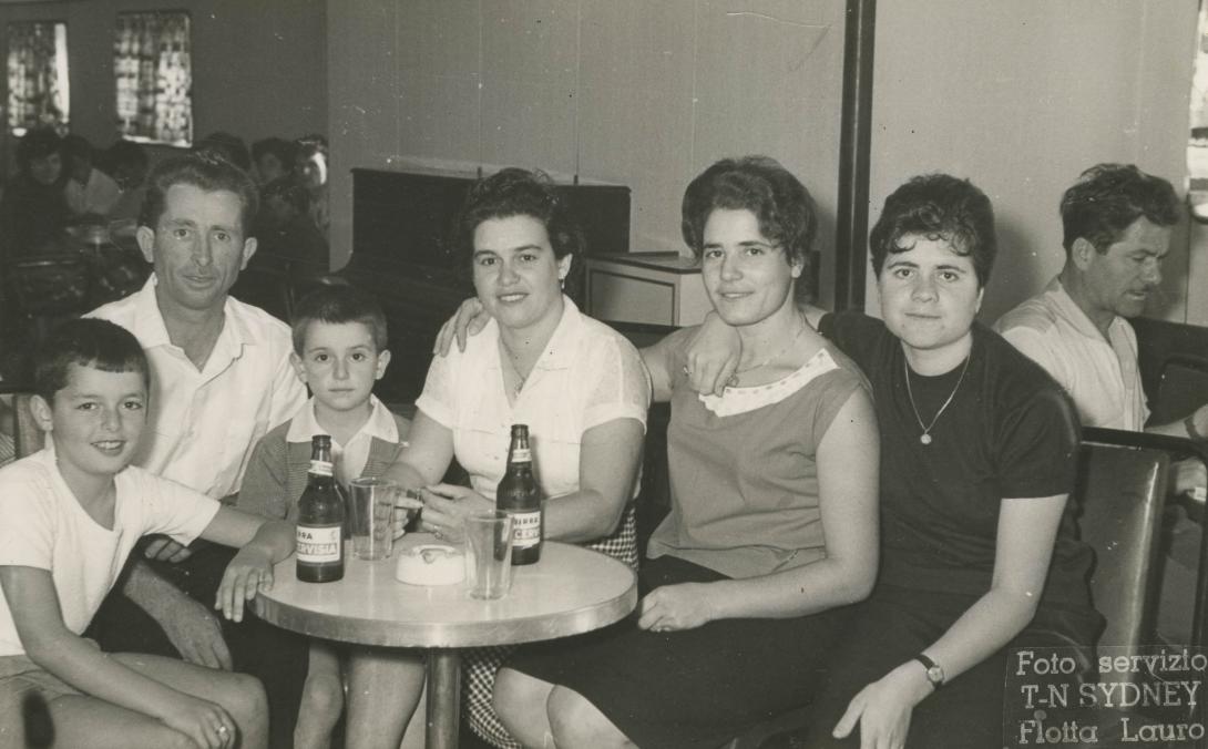 A group of friends sitting around a small table with two Birra Cervisia bottles and an ashtray.
