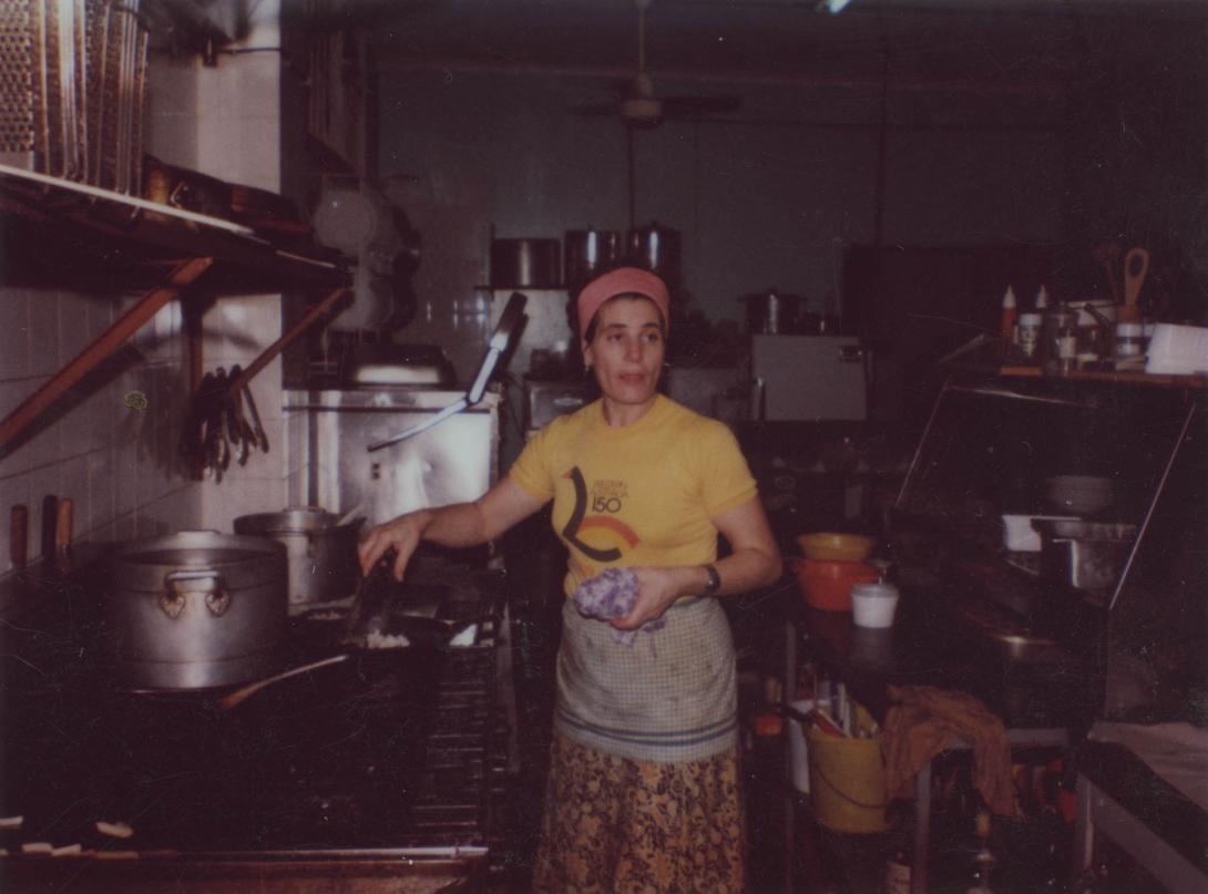 Adele wearing the iconic yellow "Western Australia 150" t-shirt, preparing food in a pan with tongs.