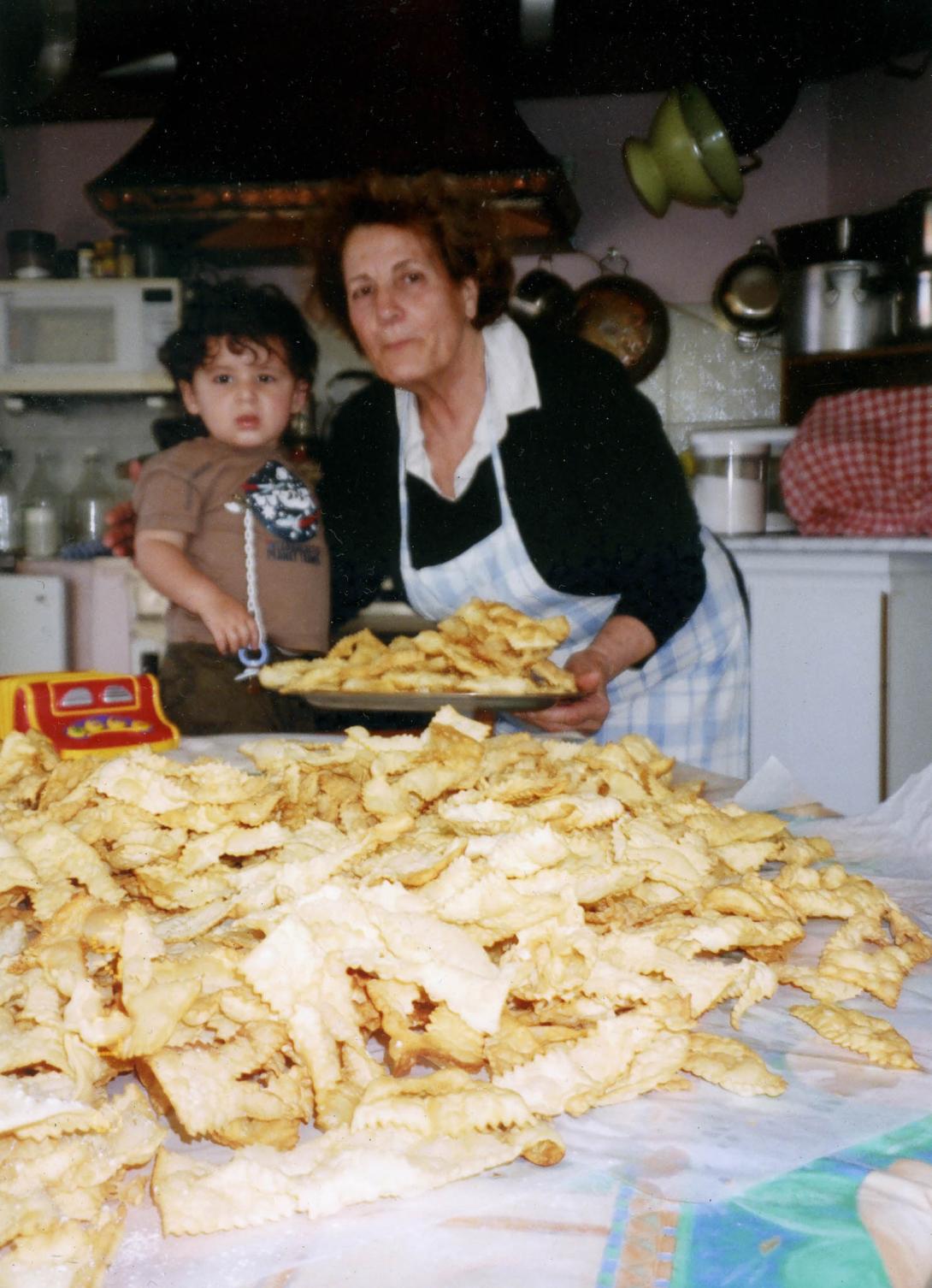 Present-day photo of Adele with a small boy, standing behind a table stacked with an enormous pile of cooked food.