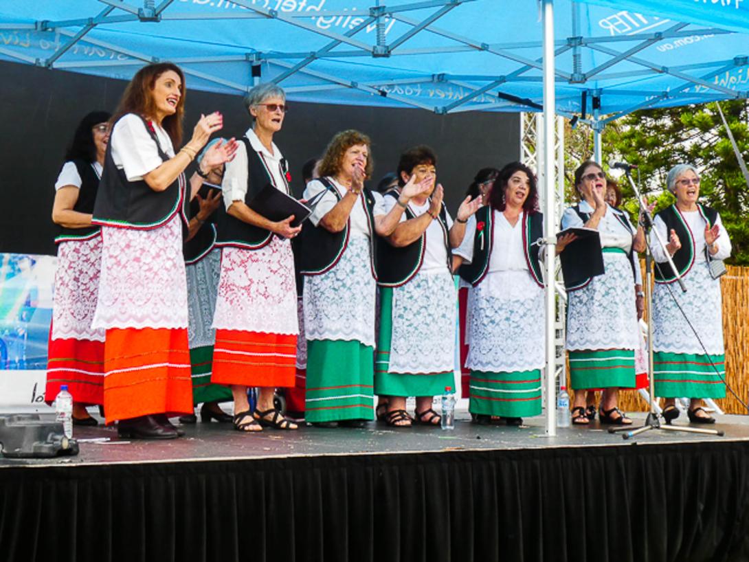 The choir clapping on stage, in white lace over green or red dresses, and black vests.