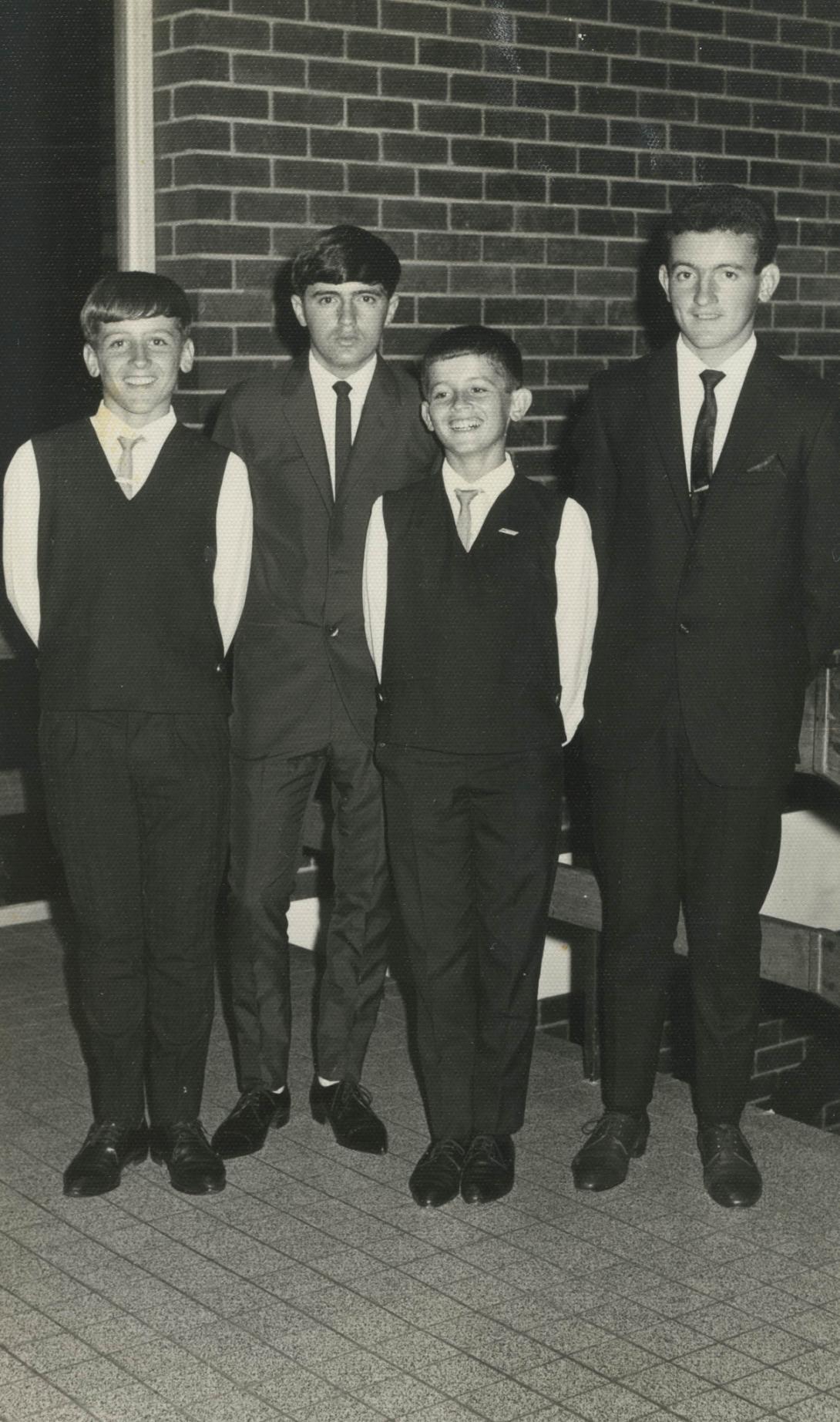 Four boys in dark vests and ties.