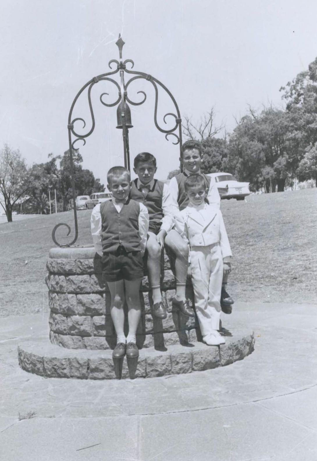 The boys in a park perched on an ornately decorated stone well.