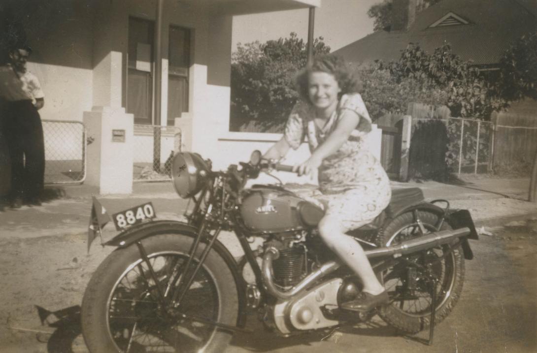 Doris in a flower print dress grins while seated on the "Ariel" branded motorbike.