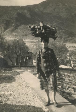 Vittoria smiling at the camera with firewood balanced on her head.