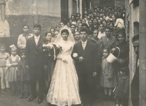 A large crowd in a narrow street standing behind the married couple.