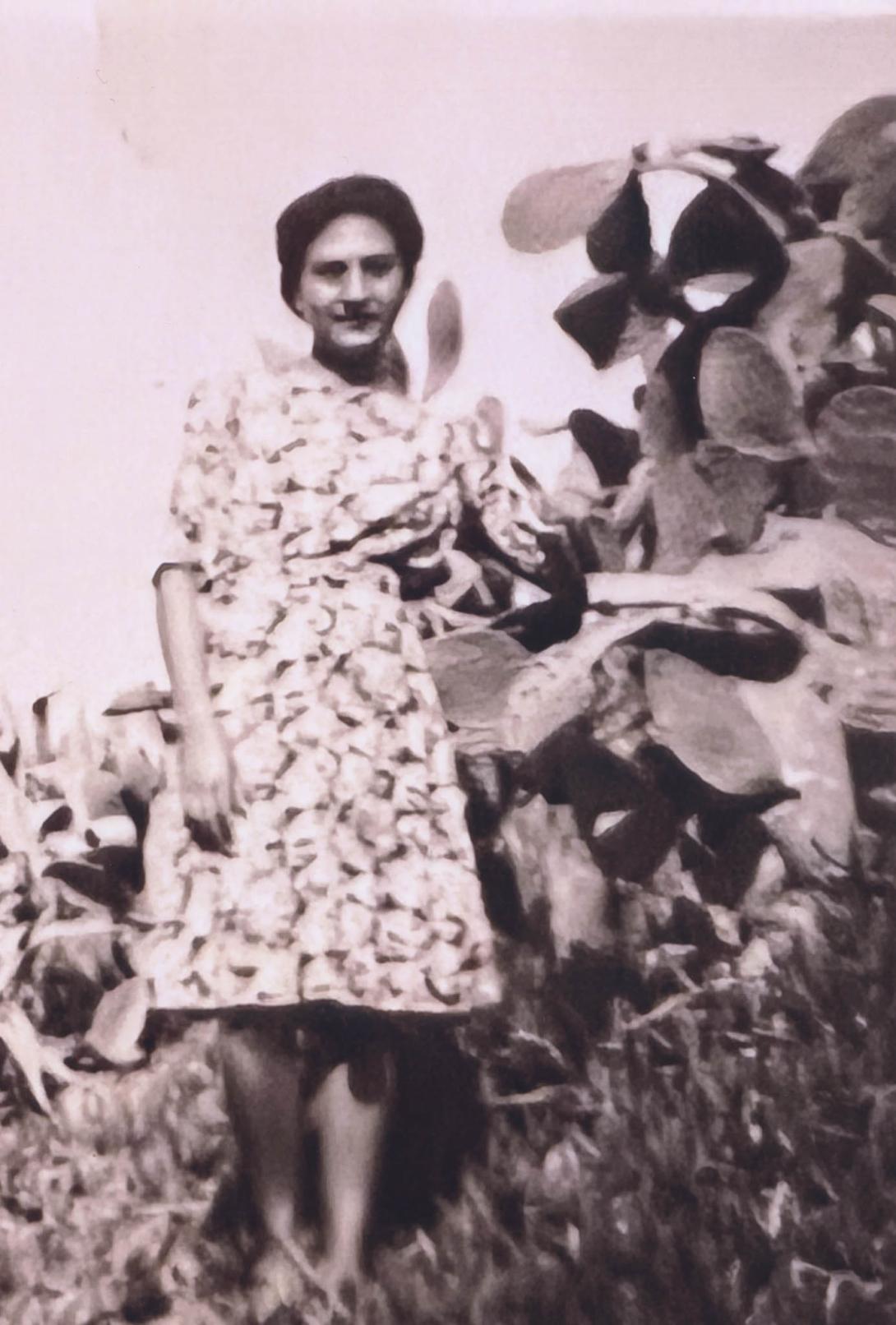Old blurry photo of Rosa in a flower print dress, beside a plant that is bigger than her.
