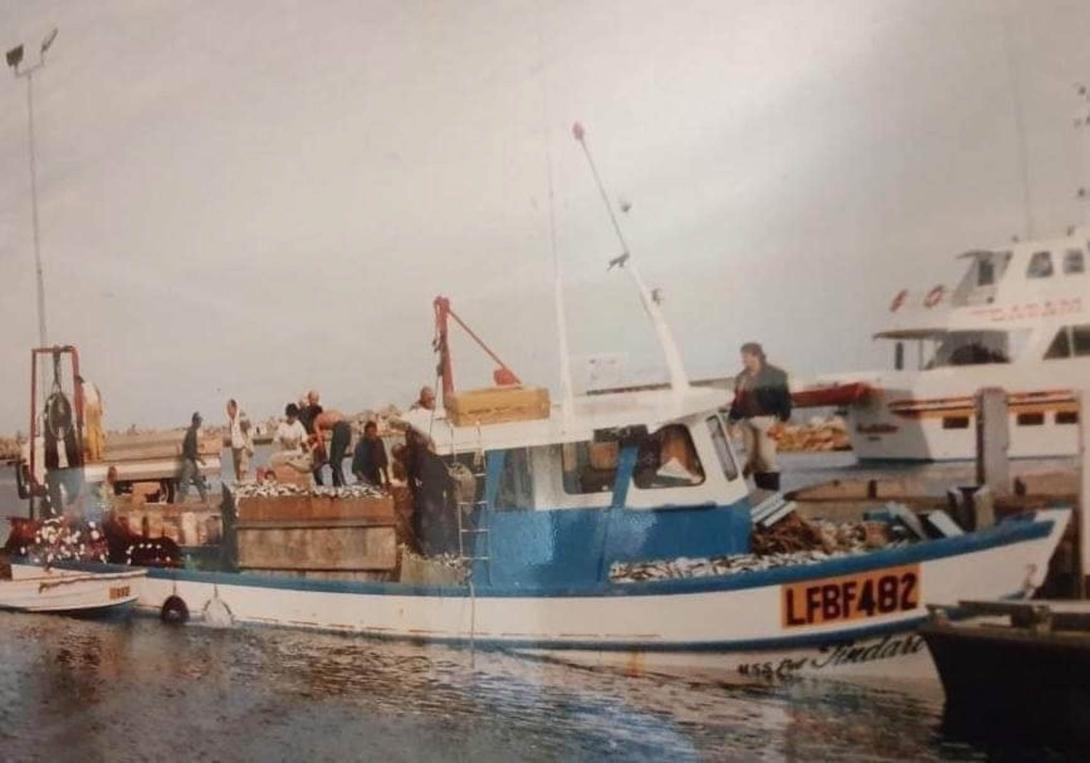 A small blue boat, its deck piled with fish.