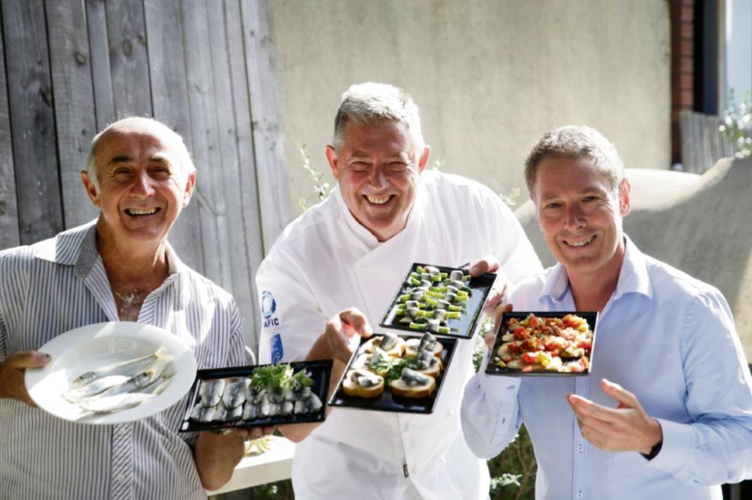 Glossy promotional photo of the three smiling men holding trays of food.
