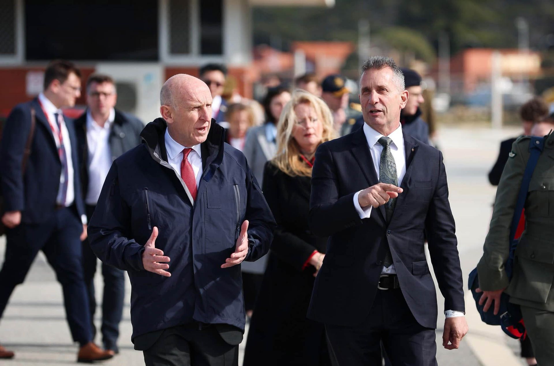 Two men wearing suits in an important discussion as they walk a busy street.