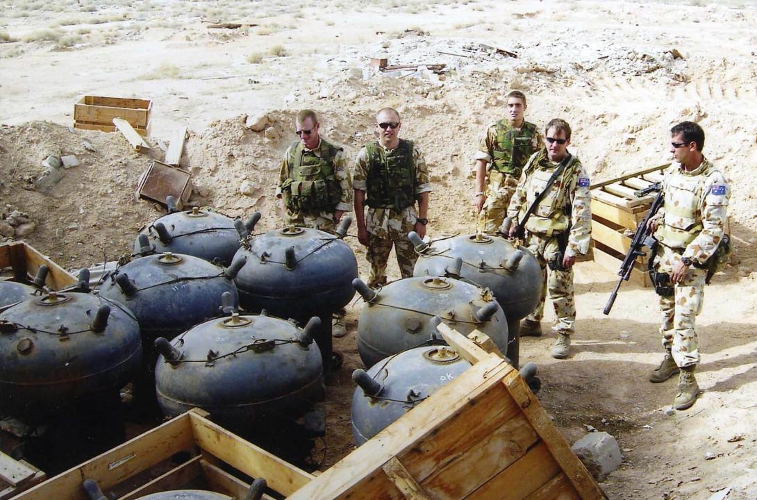 A group of men in military fatigues next to unexploded naval mines.