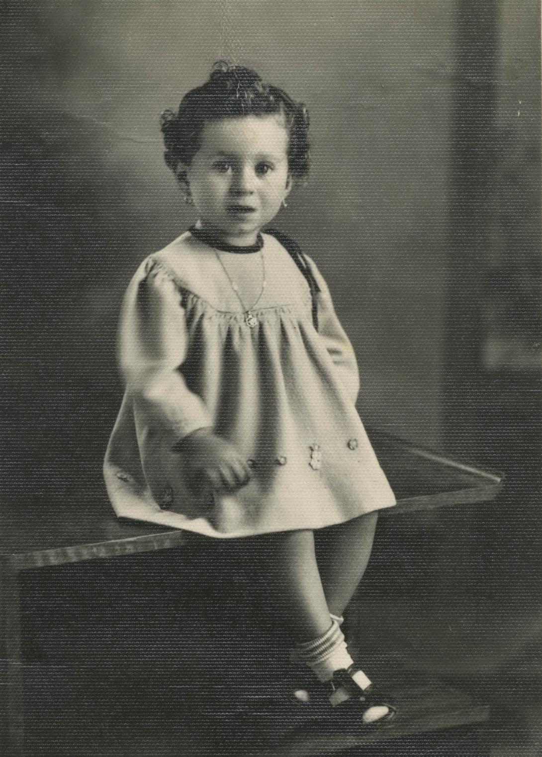Studio portrait with Carmela in a white dress, looking curiously at the camera.