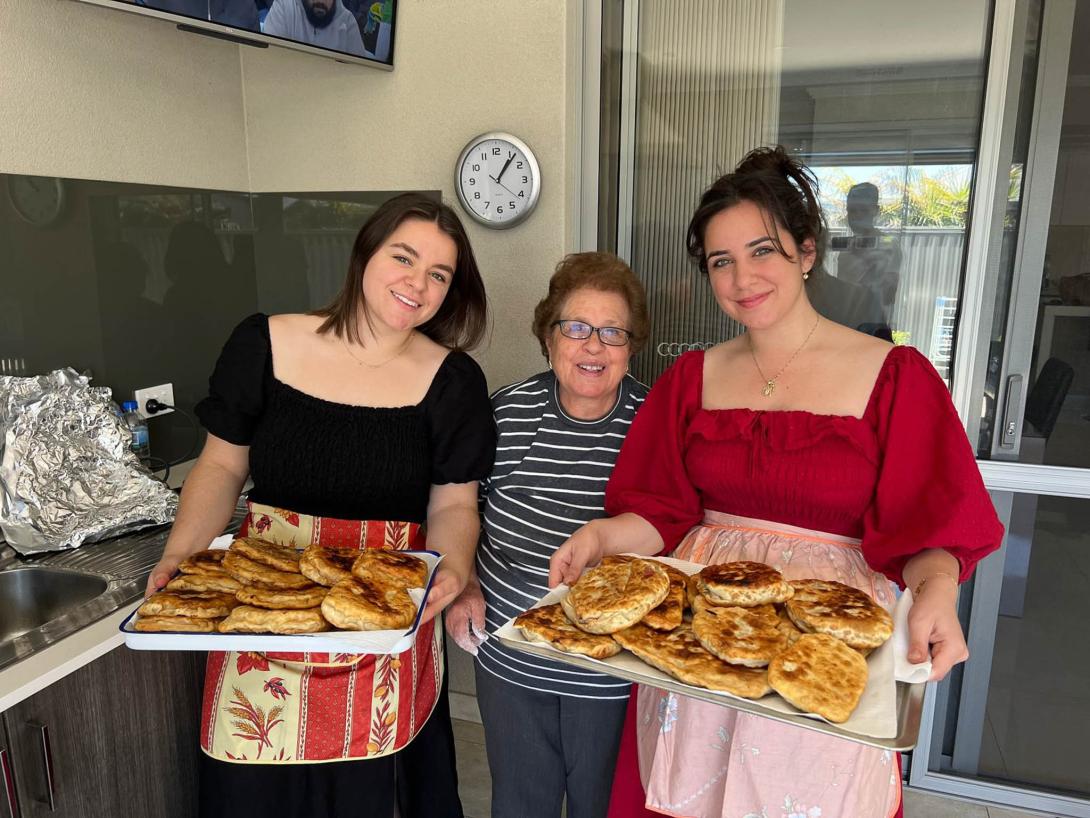 The granddaughters hold two huge trays of baked goods.