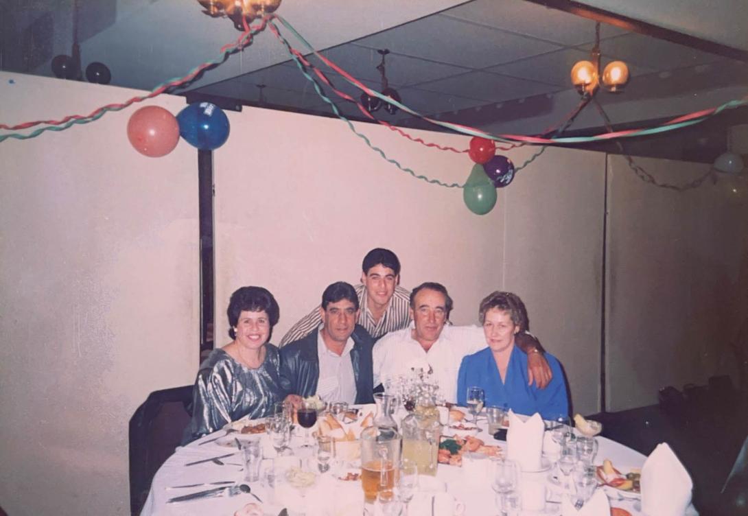 The table is covered with food and drink. There are colourful balloons and streamers on the ceiling.