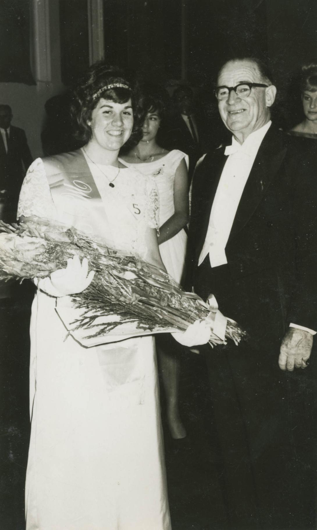 A beaming Louisa in a sash holding a big bouquet.