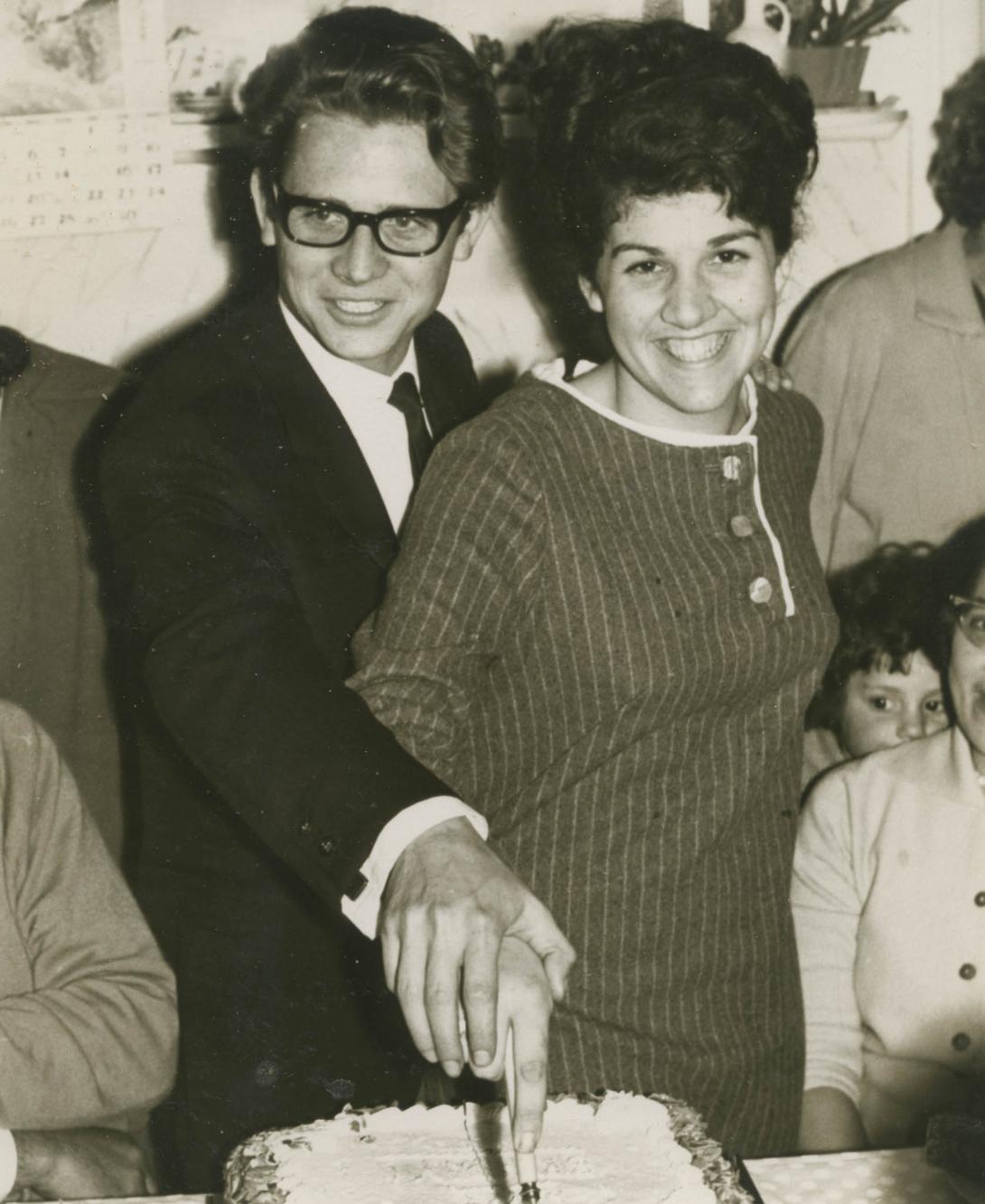 Stellario's hand is on top of Louisa's as she holds the knife, cutting into the cake together.
