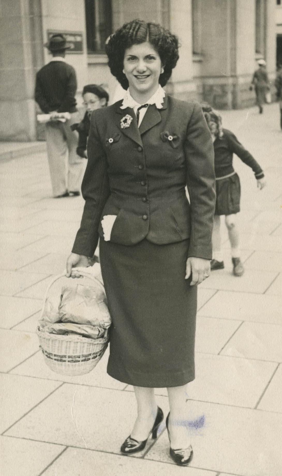 Betty wears a dark business suit and carries a basket.