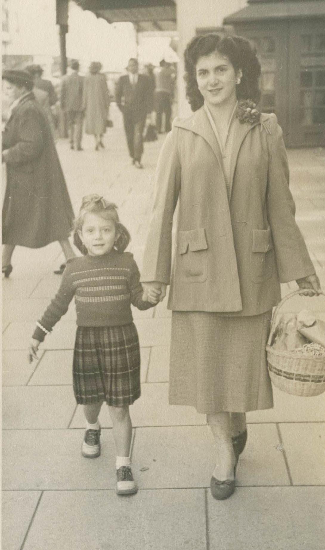 Mother and daughter hold hands on the busy street.