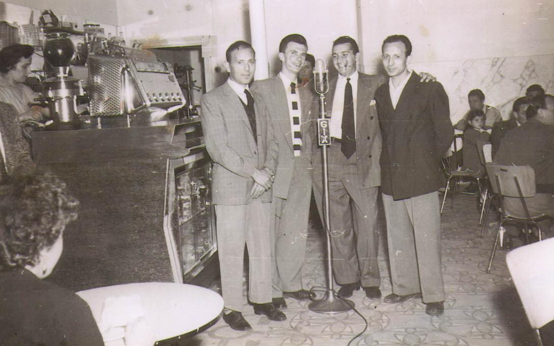 Four men crowd around one microphone on a stand in the middle of the store.