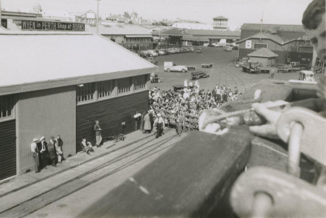 A crowd gathering at one of the harbour's sheds. A sign reads "When at Perth shop at Boans."