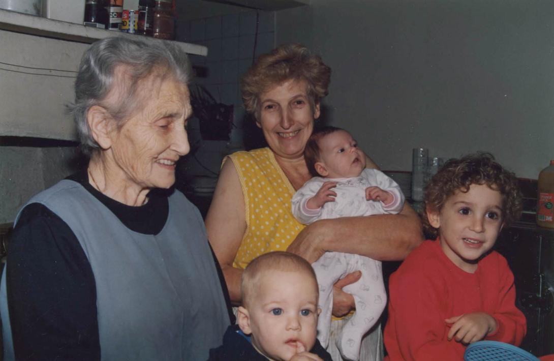 Maria smiles holding a baby as the other young children look at someone off-camera.
