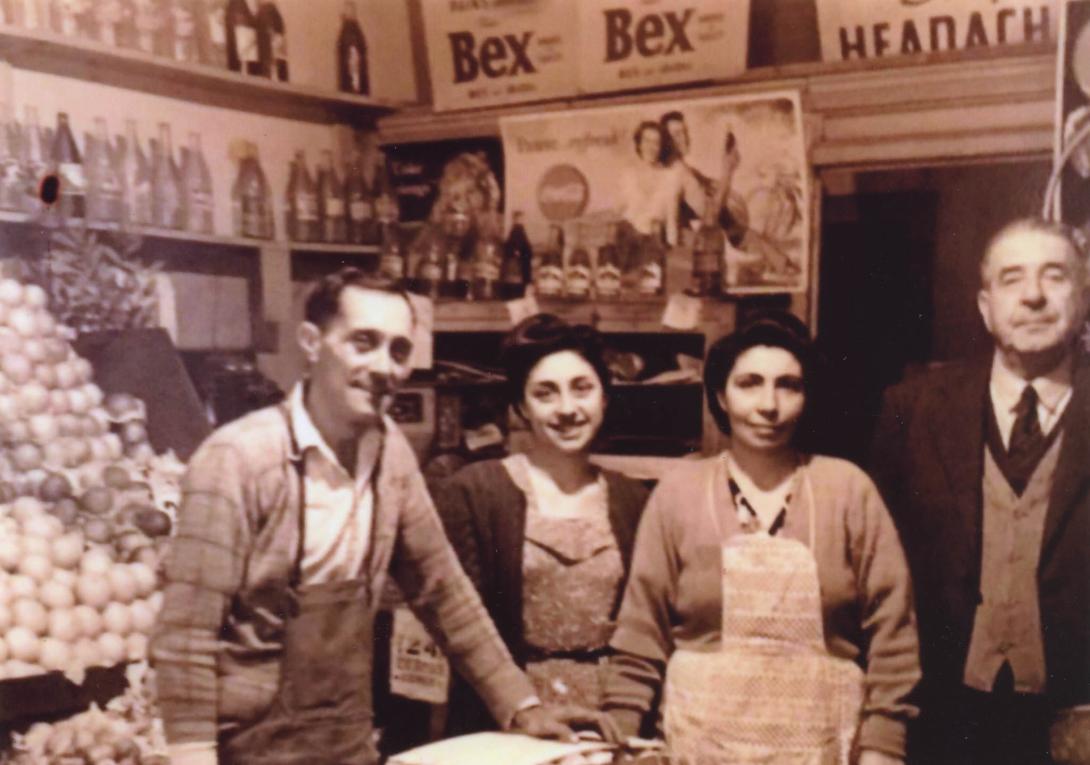 Behind the family is a large pile of onions. There are posters on the wall advertising Coca-Cola and 'Bex' pain medication.