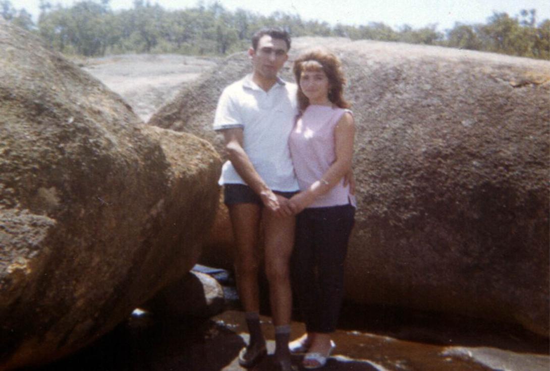 The couple hold hands between some large boulders as they take a break from hiking.
