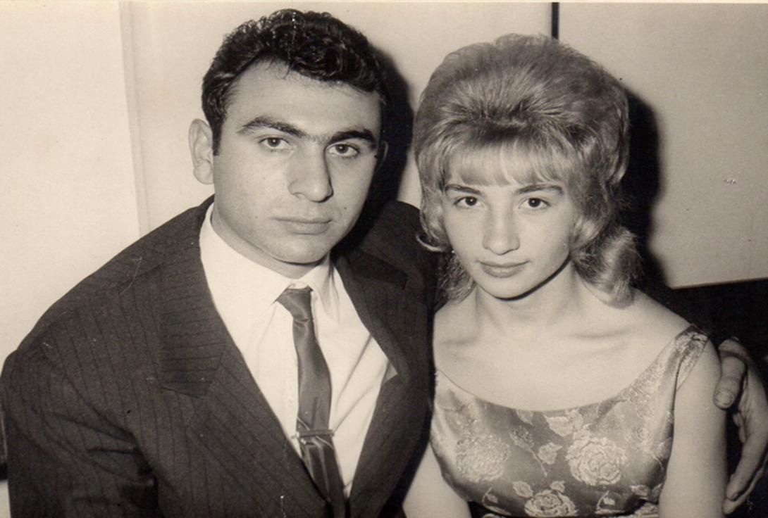 The couple are seated in an embrace, hair done up and dressed stylishly.
