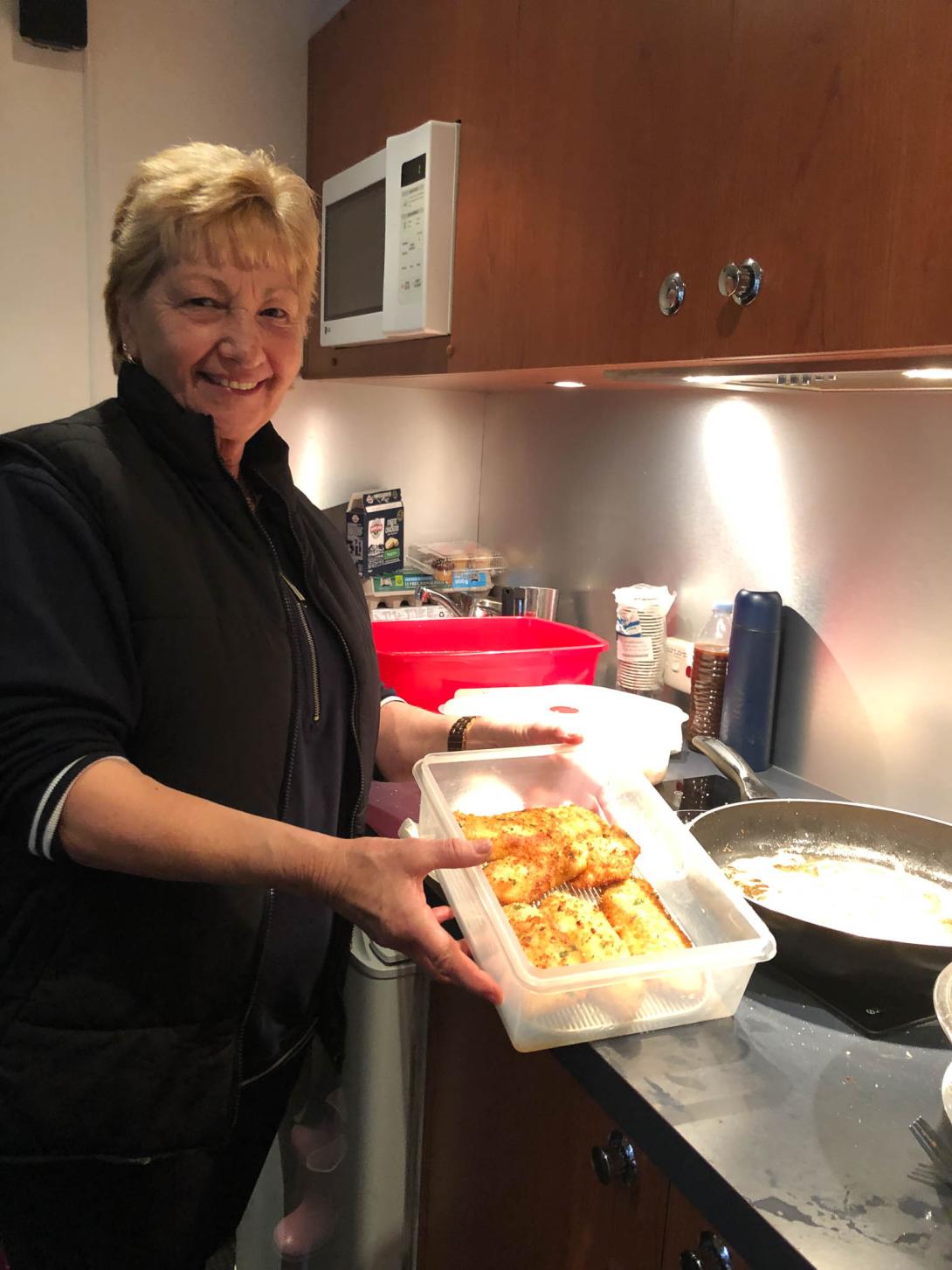 Maria shows a Tupperware dish of cooked food to the camera.