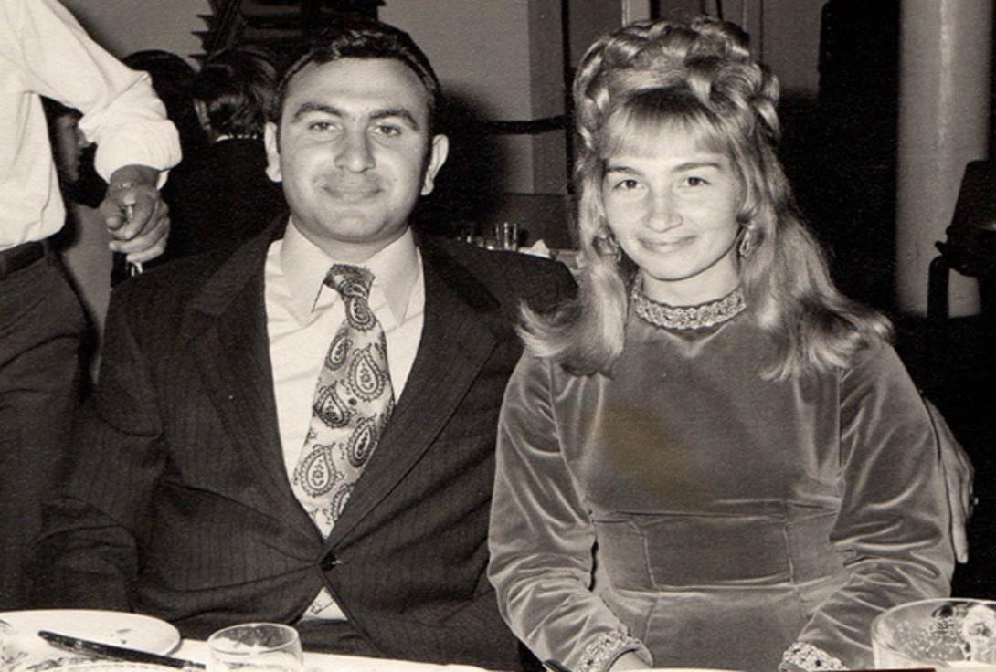 Basil wears a dark suit and wide, brightly patterned tie. Maria's hair is lavishly done up.