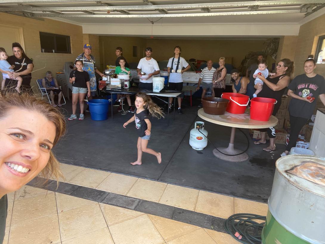Many family members gather around tables stacked with big tubs of sauce for a group 'selfie.'