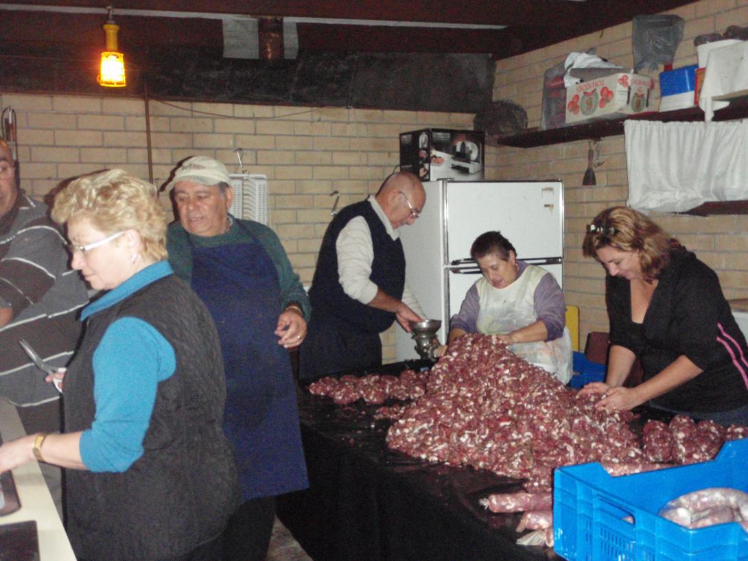 Family members of different ages work at a trestle table covered with a mound of minced meat.