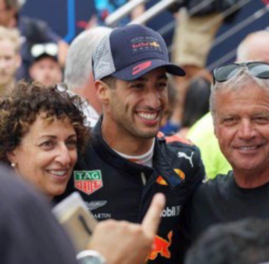 Daniel in racing uniform and cap greeting people at the racetrack stands.
