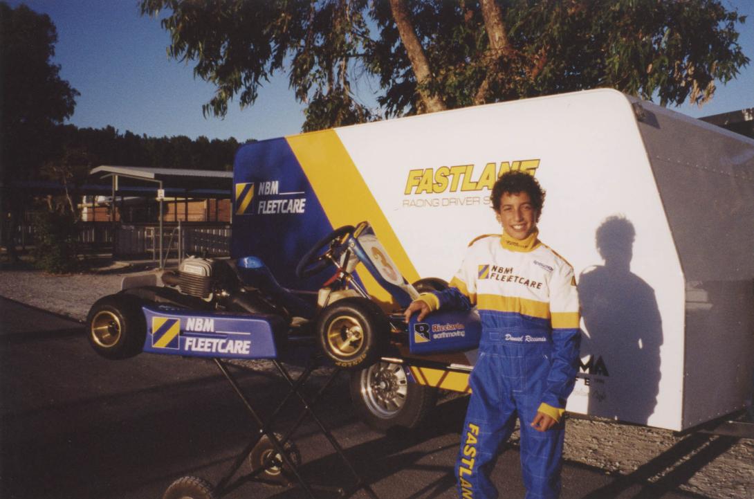 A younger Daniel in racing suit next to a Go-kart and trailer.
