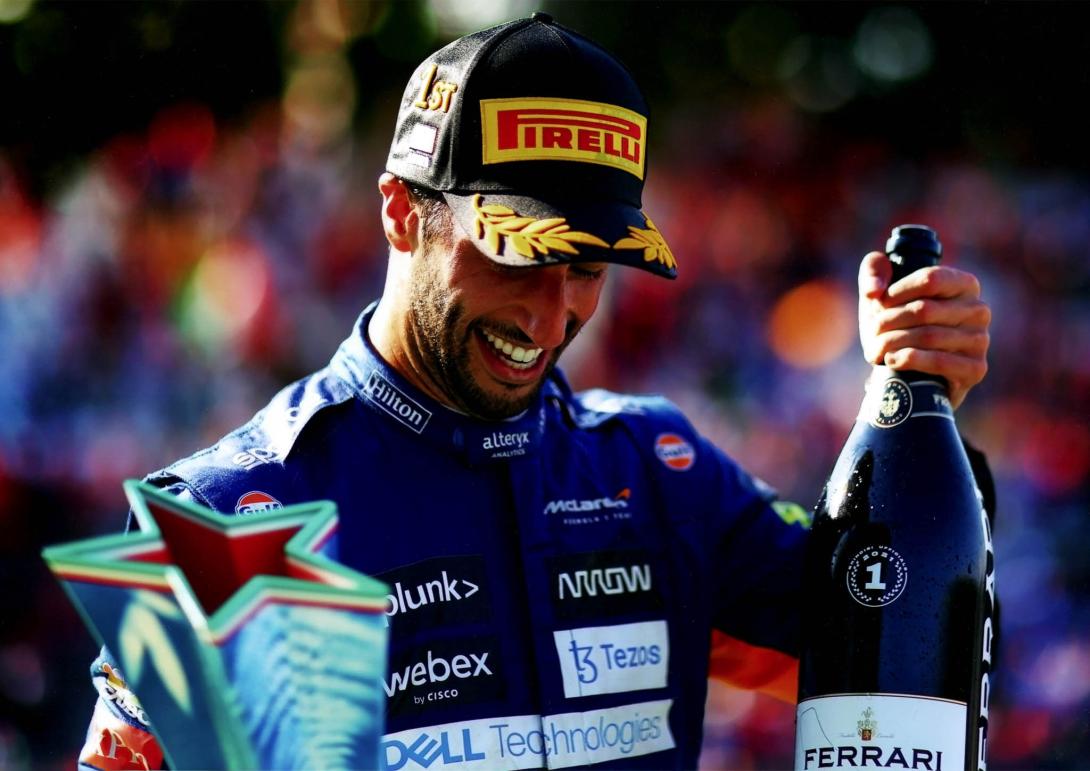 Daniel grinning while holding up the trophy and bottle.