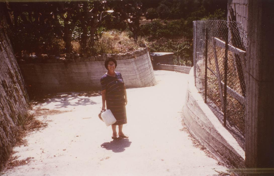 Paola on a path holding a plastic water jug.