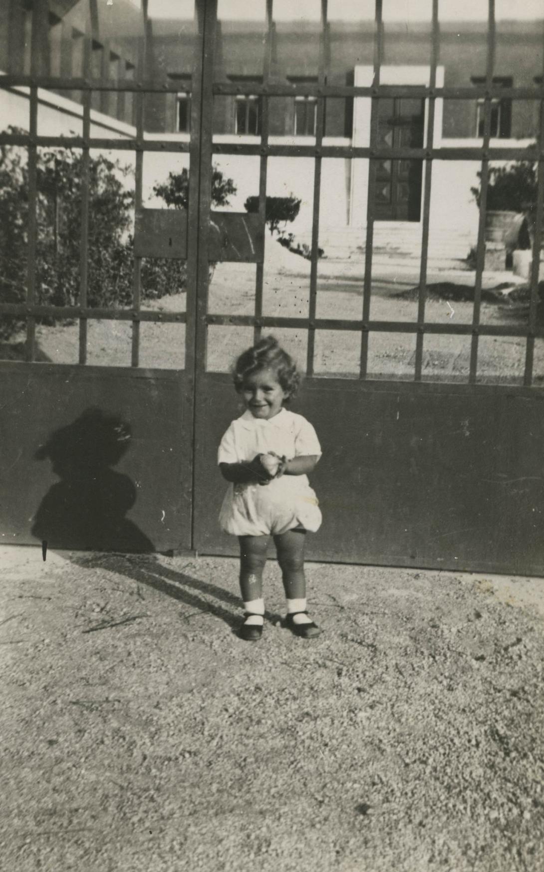 Franca has a cheeky grin, standing in front of a large metal gate.