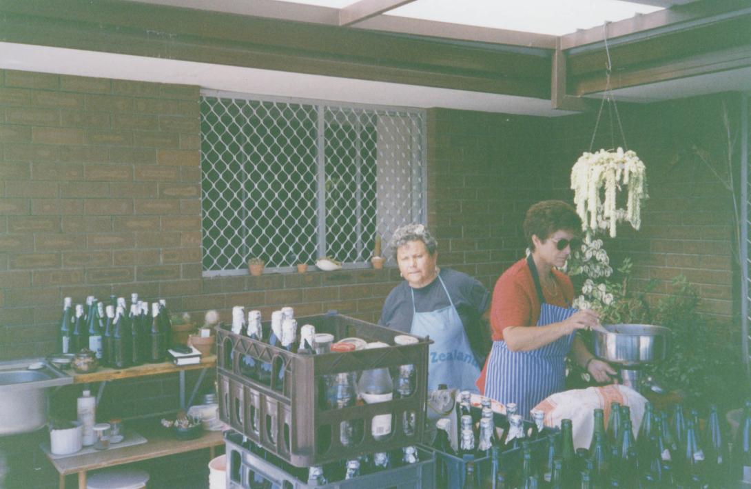 Franca stirs a big pot behind many crates filled with drink bottles.