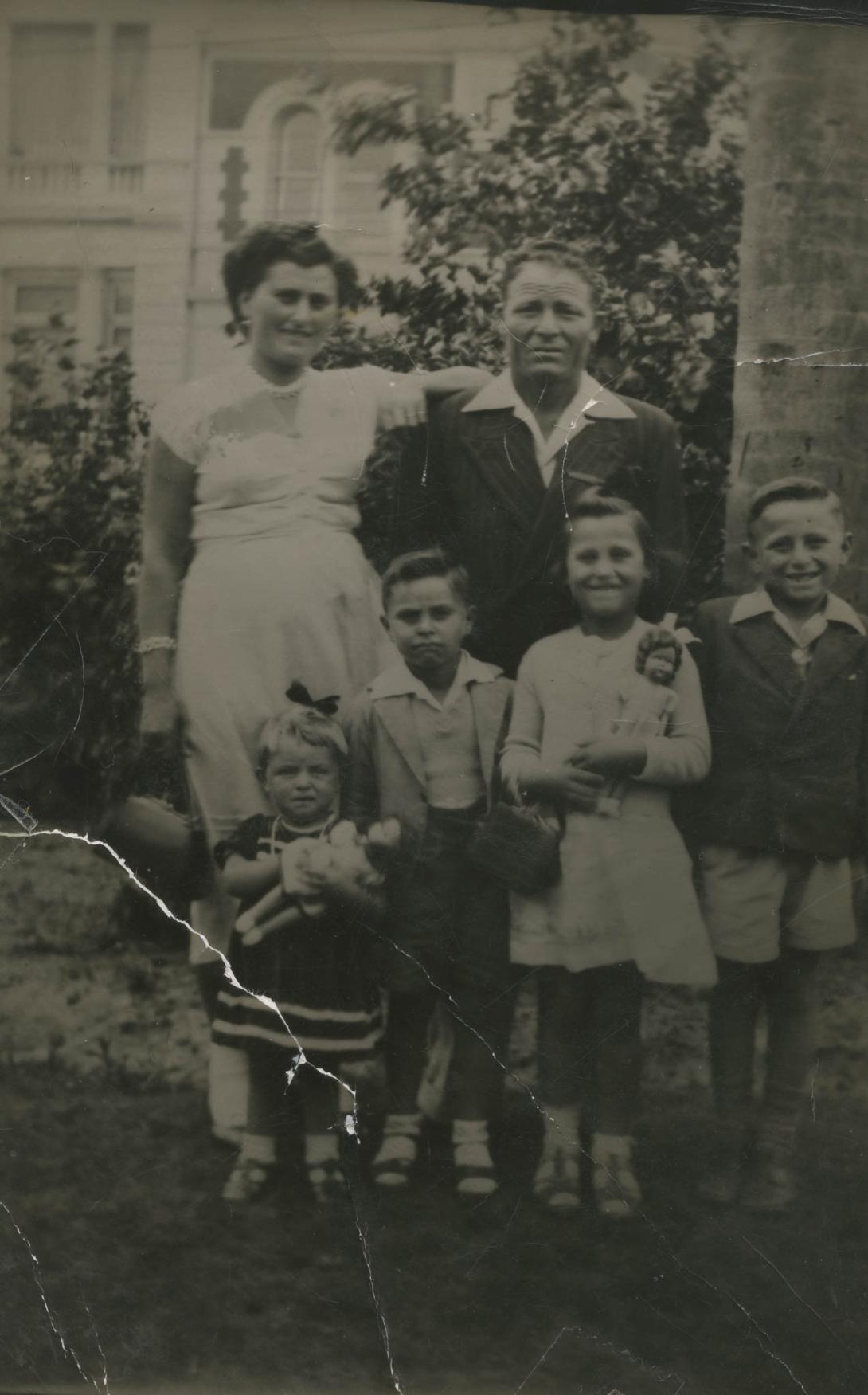 There is a tear in the corner of this old photo, two of the children happily clutch dolls to their chests.