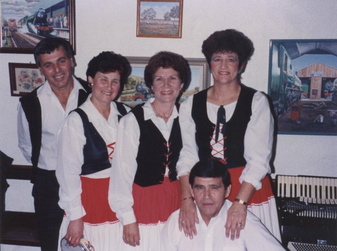 The group smiling in traditional white shirts and black vests.