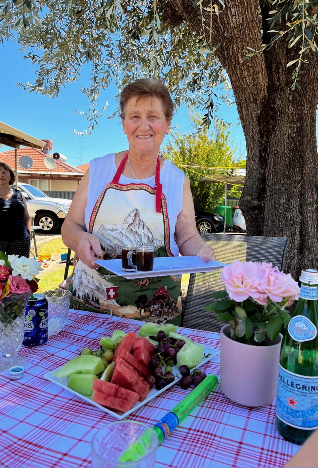 Rosie in an apron with some drinks on a tray and fruit on the table.
