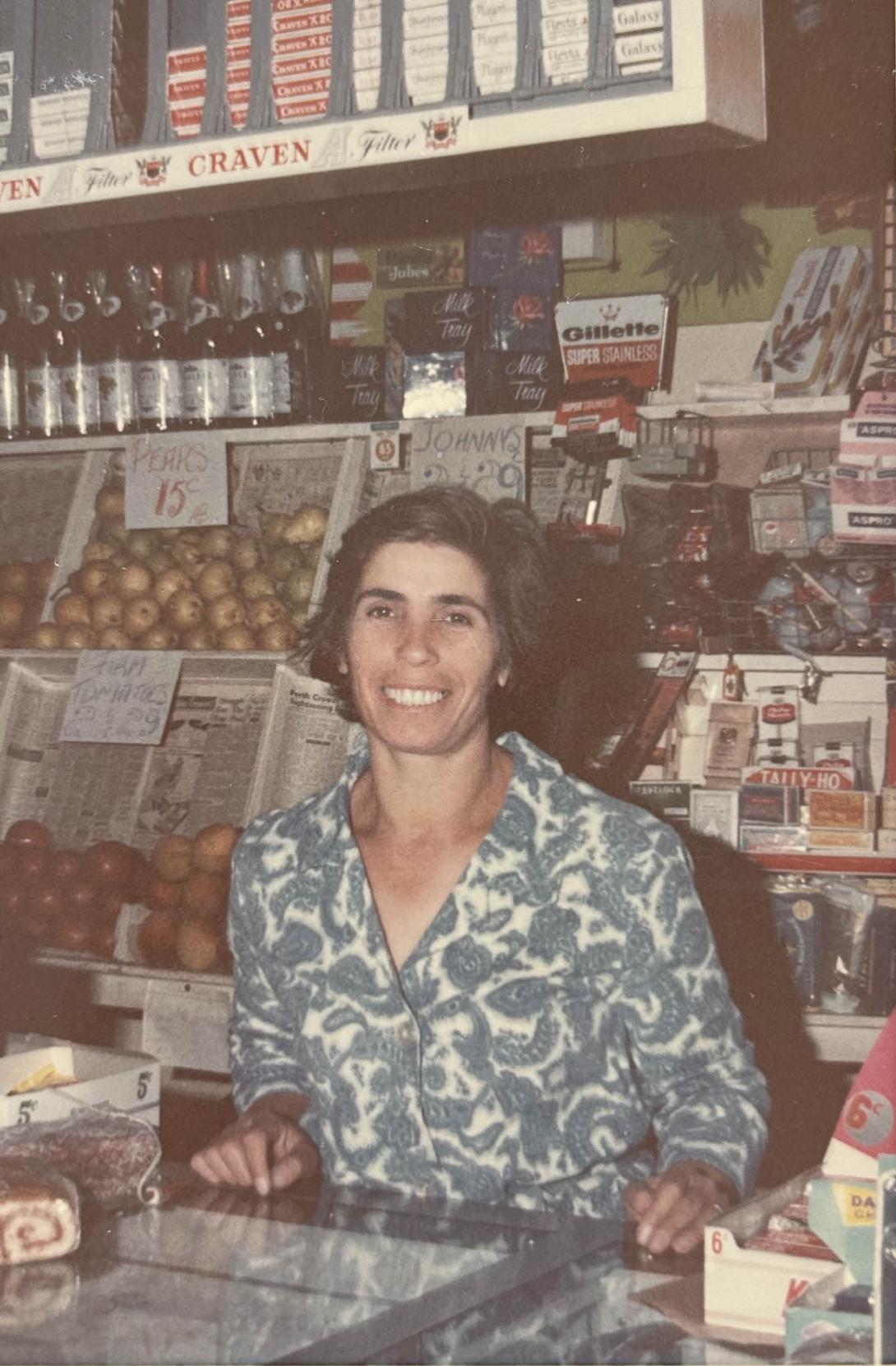 Behind the shop counter with Carolina are stacks of pears and tomatoes, beer bottles and packets of cigarettes.