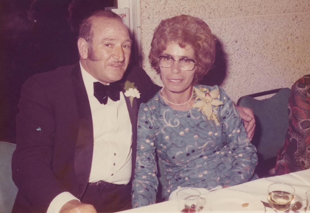The well-dressed couple seated closely together at a table.