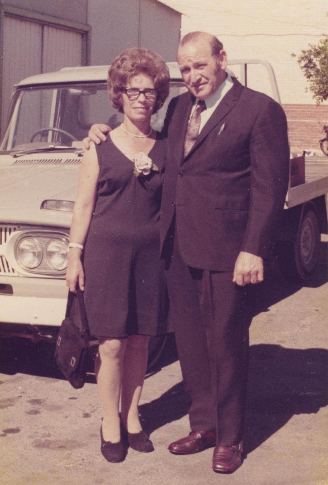 The couple dressed in black stand together in front of a truck.
