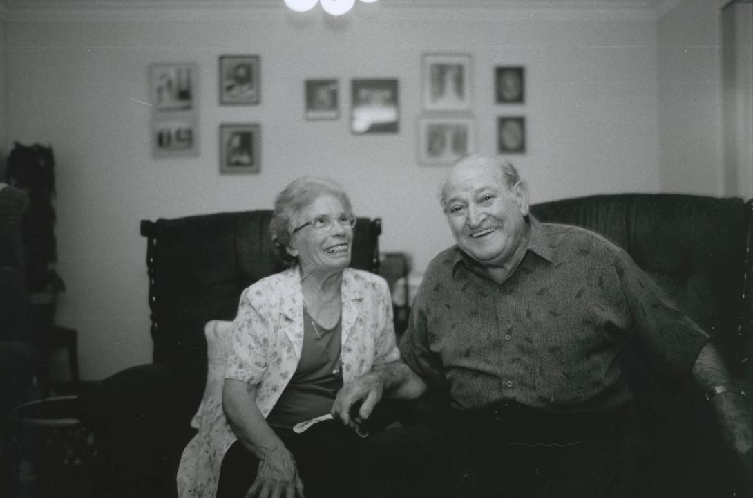 The couple share laugh on the couch. Family portraits are on the wall behind.