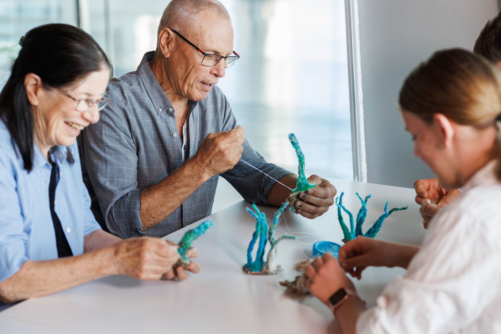 A small group are shown sewing ghost net materials into marine fauna project elements for a Maritime Crafternoon ghost nets art activity workshop.