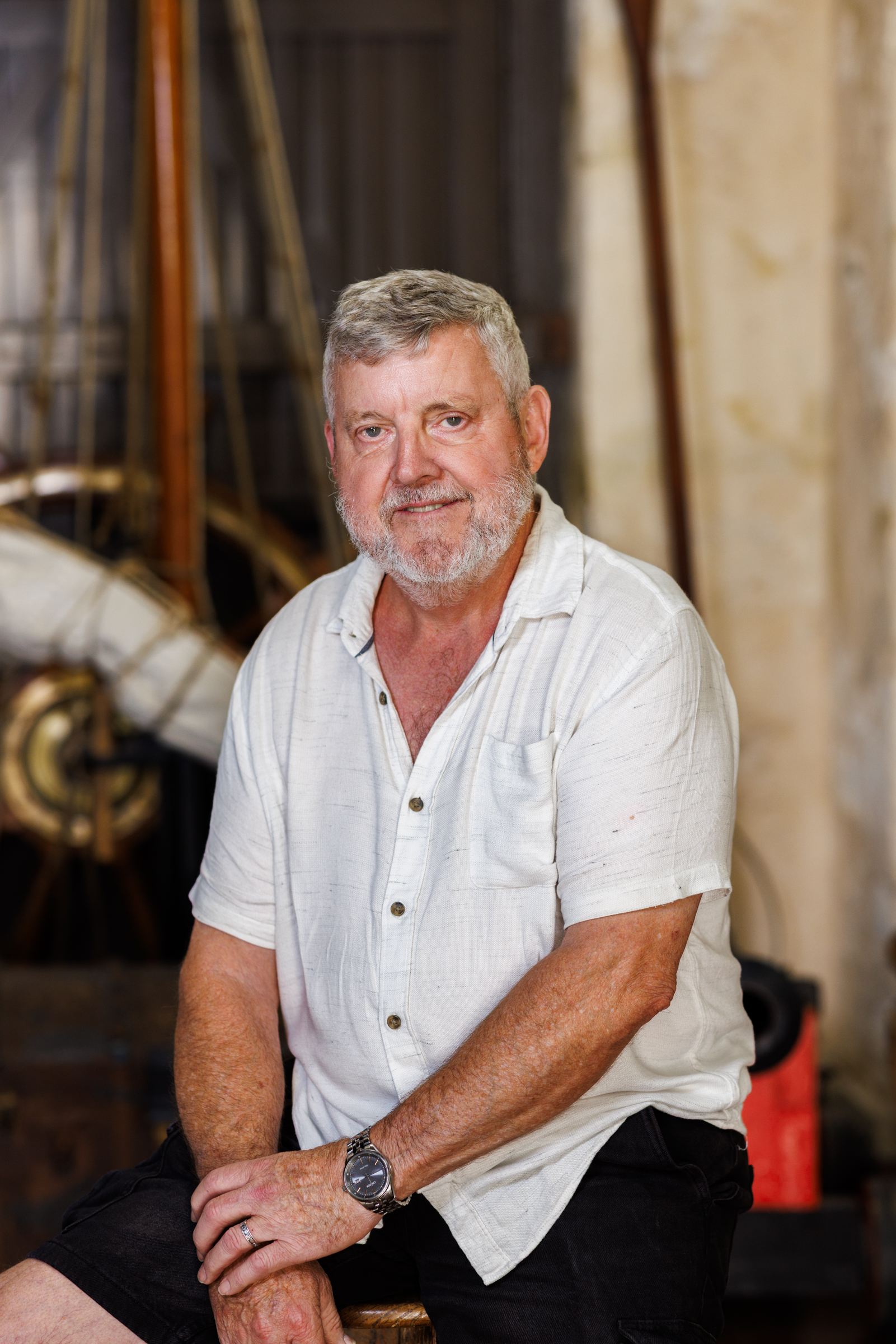 a an adult man sits on a stool smiling with nautical themed props in the background