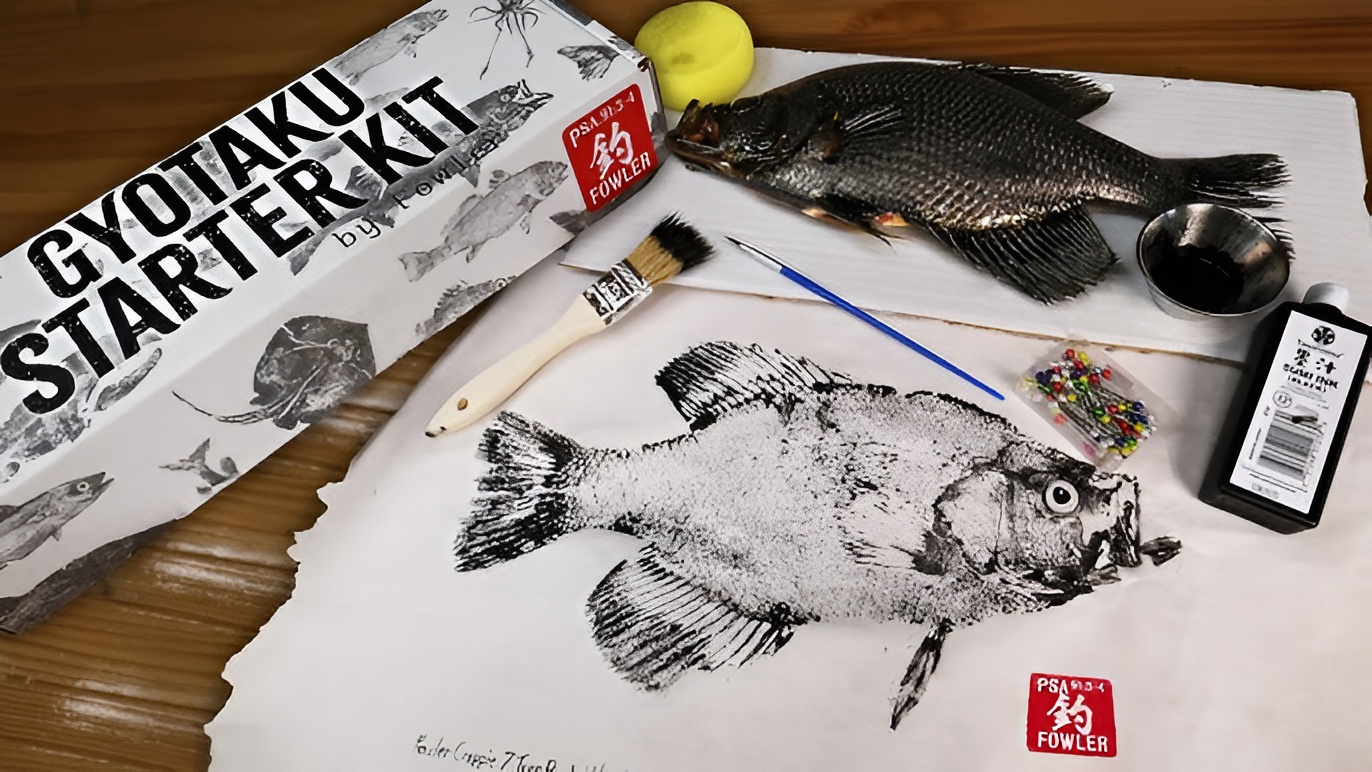 a top view of a table with a fish print and a fish with materials used to create the artwork