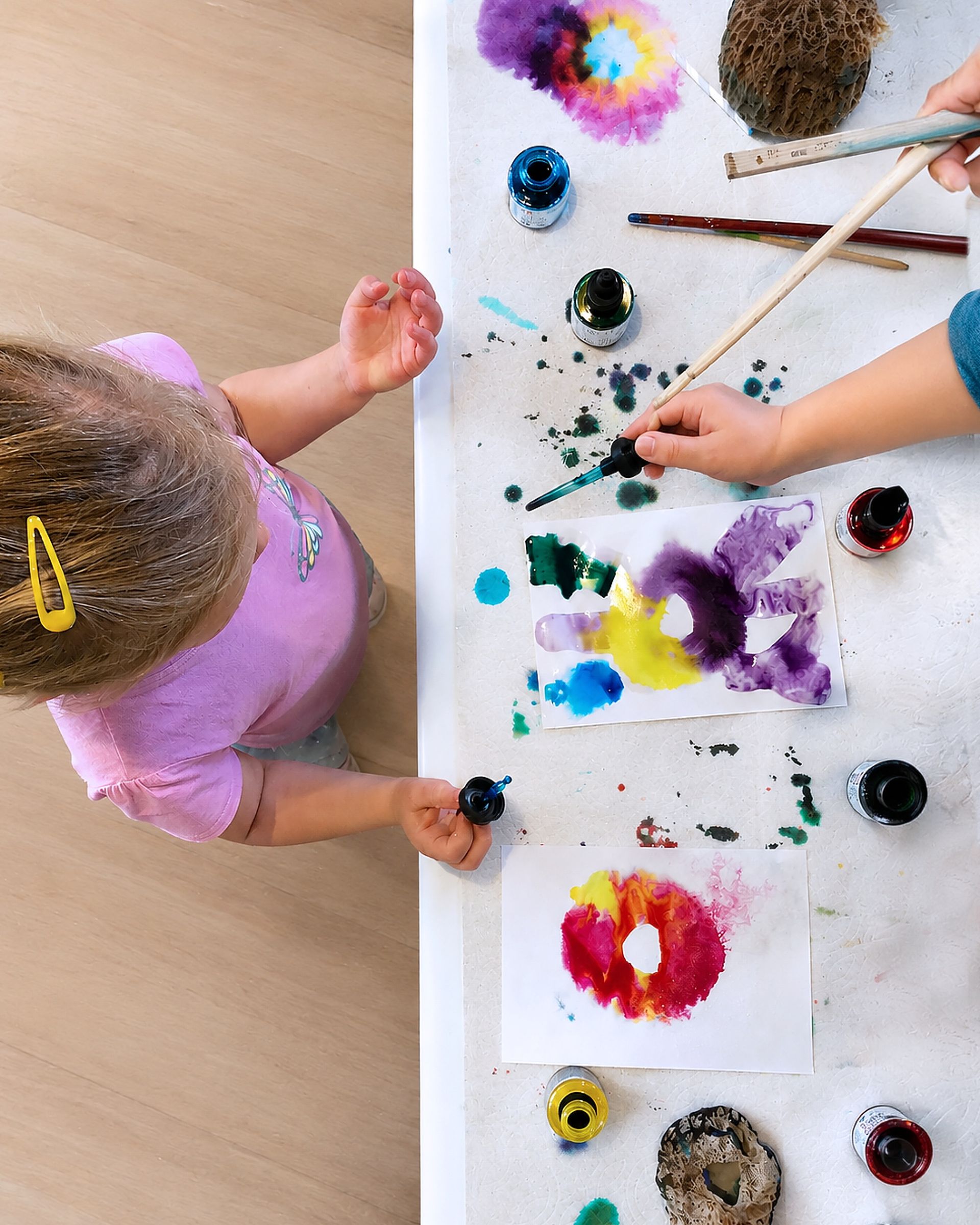 topdown view of an activity table with paints, ink and artwork where a child approaches the table to take part